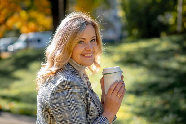 Portrait of lovely blonde in gray with blue shade of sandpaper holding cup of coffee in city park. Autumn day in nature. Happiness and peace. Life in moment. Walking in fresh air. Coffee break.