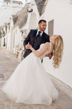 Mutlu ve neşeli romantik çiftin dikey portresi, sarışın kadın eğilimli ve siyah saçlı adam düğünden sonra, aşırı giyinmiş, kucaklayan, dans eden, antik İtalyan evlerine karşı