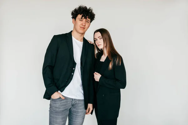 Portrait of young attractive dark-haired curly man and long haired woman in black outfit, sanding close. Female touching shoulder, bound and love relationship couple. Studio shot on white background.