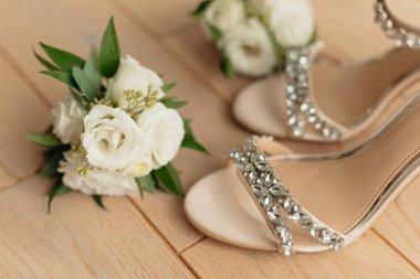 Seçkin, topuklu kadın ayakkabıları ve odada gelin için bir buket taze beyaz gül. Kadın aksesuarları, yakın plan, bej arka plan. Gelinler sabah, düğün hazırlıkları, ayakkabı provaları..