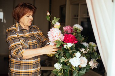 Koyu renk saçlı, kareli gömlek giyen, pembe, beyaz gül buketi püskürten, çiçekleri düzelten yaşlı kadınların yan görüntüsü. Çiçekçi, anneler günü, kadınlar günü, evlilik yıldönümü.. 