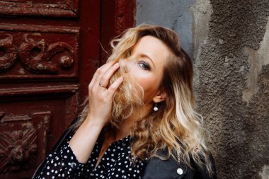 Modern, ciddi, tarz sahibi, siyah deri ceketli, makyajlı, kapıya bakan sarışın kadın. Şehir tarzı. Ayrılma ilişkisi, yüzüğü olan bir kadın el ele tutuşur.