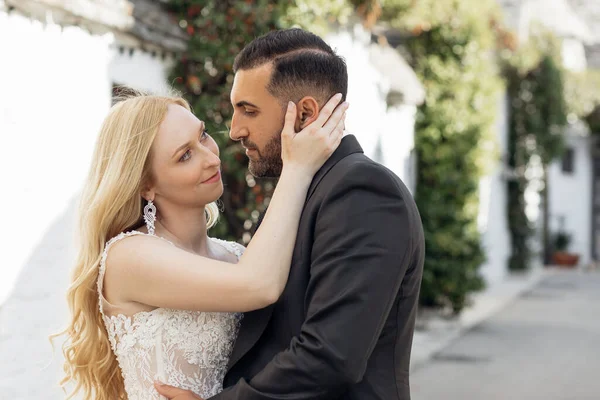白いドレスを着た若いブロンドの花嫁とスーツを着たブルネットの新郎の肖像画は イタリアの街の通り 都市の背景でお互いを受け入れ 見ています 美しくロマンチックな結婚式幸せなカップル — ストック写真