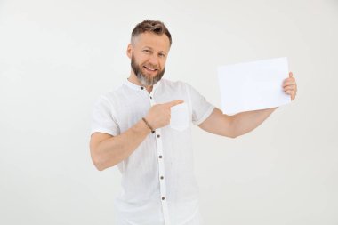 Sakallı, gülümseyen bir işadamı, beyaz, boş bir kağıt parçasını gösteriyor, kameraya bakıyor, beyaz izole arka plandaki stüdyoya bakıyor. Model yap, mesaj için yer aç. Promosyon kariyeri. Boşluğu kopyala