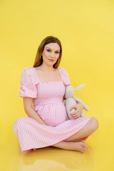 怀孕后期腹部的女人穿着休闲装坐在地板上 抱着柔软的玩具 黄色背景 年轻孕妇怀孕的画像 快乐怀孕和母性概念 — 图库照片