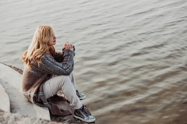 Νεαρή Ξανθιά Γυναίκα Ζεστά Ρούχα Κάθεται Στην Όχθη Του Ποταμού — Φωτογραφία Αρχείου