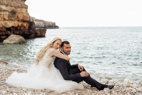 結婚式のドレスと公式のスーツの夫婦は崖の岩の山の近くの海や海の海岸に座っている ヨーロッパ イタリアの海外新婚旅行 お互いを抱き合って 愛の境界線 イベント — ストック写真
