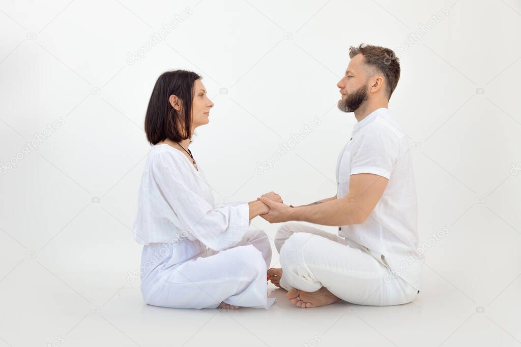 Man and woman, couple in love, wear white outfit, practice Pilates and yoga, sit in lotus posture, look each other, holding hands together. Healthy lifestyle, spiritual trust and conscious tantra love