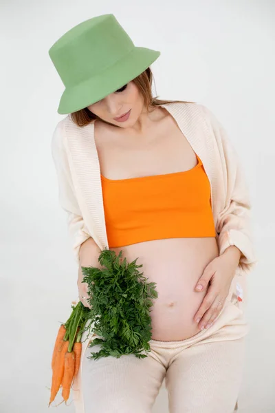 pregnancy, healthy food and people concept, close up of happy pregnant woman with carrot in hands on white background