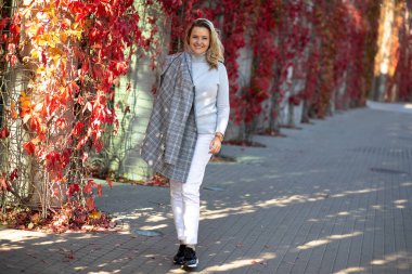 Açık renk pantolonlu, kaşmir kazaklı ve omzunun üzerinden süzülen açık gri tüvit ceketli çekici sarışın sonbahar caddelerinde yürüyerek yürüyor. Sonbaharın parlak renkleri. Şehir manzarası..