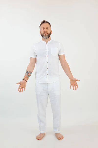 Vertical handsome barefoot man in white outfit on isolated background. Show open arms welcome pose. Sport activity, healthy lifestyle. Yoga instructor, coach, Asana and trust exercise. Copy space