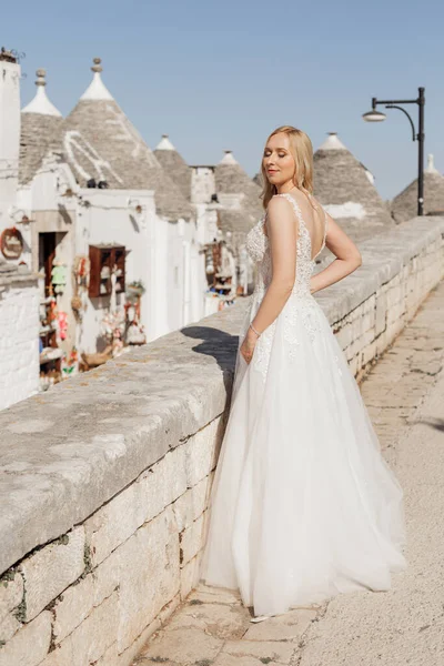 Vertical pretty blond woman, bride on her wedding standing alone, close eyes, stylish, fashionable female in wedding dress. Posing against historical center of Italy with roofs pyramids, Italy sky