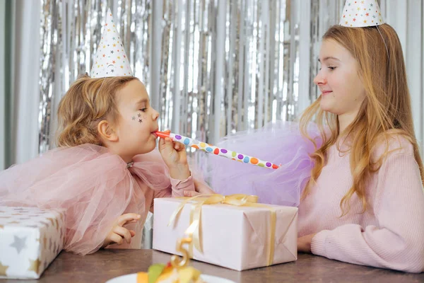 İki tatlı kız kardeş, 5 yaşına giren en küçük kızın doğum gününü kutluyor. Kızlar kornayla eğleniyor. Önlerinde hediye kutuları ve pasta var. Festival etkinlikleri organizasyonu. 