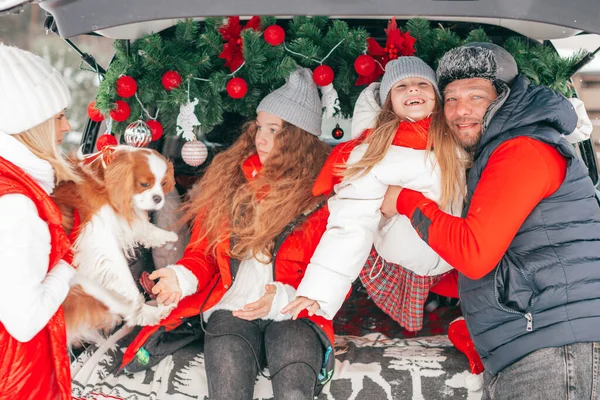 Adorable family with two daughters inside of family car trunk. Happy healthy people, children and dog in winter red fashion clothes having Xmas party, traditional celebration, Christmas moments
