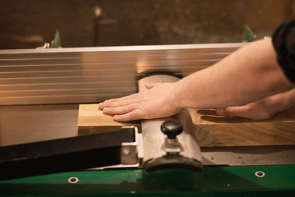 Close-up of carpenter hands in work process, pressing, fix and work accurate with wood cutting machine in the workshop, making shape, hewing of wooden bar, timber by metal slab, tool on grinder part.