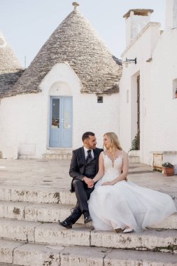 Dikey portre sevdalısı, neşeli romantik çift, sarışın kadın ve siyah saçlı adam aşırı giyinmiş, el ele tutuşuyorlar, birbirlerine bakıyorlar, tarihi eski evin merdivenlerinde oturuyorlar, İtalya,