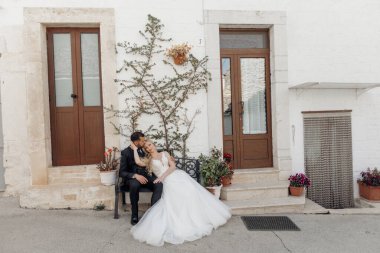 Düğün portresi, birbirine aşık evli bir çift kapıların yanındaki bankta oturuyor, beklenti, sarılma, sıralarını bekliyorlar. Tören ve kutlama. Bitkiler ve ağaç dalları açık havada duvarda..