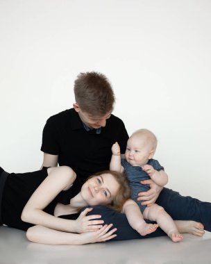 Genç anne ve baba siyah elbiseli bebekle oturup kucaklaşır, gülümser ve beyaz arka planda eğlenirler. Bedava fotokopi alanı ile ebeveynler ve bebek arasında hoş bir ilişki. Ailede mutluluk ve sevgi.