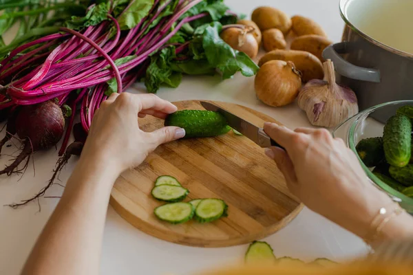 Kesme işlemi, omuzlarının üstünden kadın elleri mutfaktaki tahta kesme tahtasına bıçakla salatalık kesiyor. Sağlıklı Yeme. 