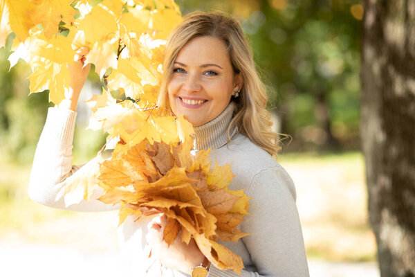 Portrait of beautiful smiling blonde holding bouquet of yellow leaves onwalk on sunny day in park. Colors of autumn. Enjoying nature. Autumn leaf fall. Wonderful moments. Beauty and health. 