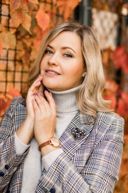 35-40 yaşlarında, güneşli bir sonbahar gününde şehir bahçesinde kızıl sonbahar yapraklarından yapılmış uzun saçlı, çekici bir sarışın portresi. Güzel kadınlar. Sonbahar manzarası. Yakın plan..