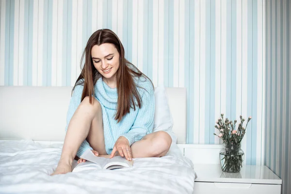 青いニットセーター読書本を着て ベッドで ライフスタイルを着てかわいい若い女性 幸せな怠惰な朝 趣味とリラックス — ストック写真