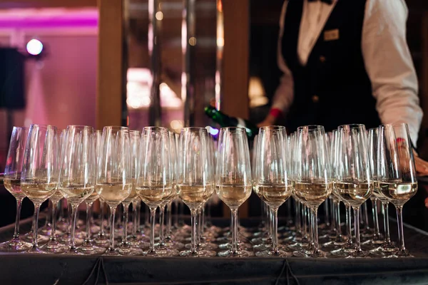 stock image Waiter serving row of glasses of white champagne on tray in restaurant closeup. Pouring sparkling wine into glasses, event celebration. Banquet hall, festive dinner, luxurious service.