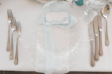 Beyaz masa örtüsü üzerinde isim için kart olan kutlama masası ayarı üst görünümü. Kimlik, dekore edilmiş salon, etkinlik kutlaması. Tatil, şık ve lüks çatal bıçak takımı ve sofra takımı, güzel servis..