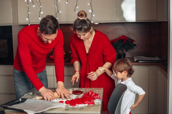 Happy family evening. Christmas Eve for young family in red clothes, father, mother and child. Son, boy 4 years old bake cookies. Homemade bakery goods, happy childhood, cozy kitchen.