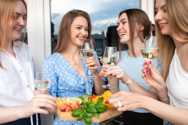 Neşeli genç kadınlar terasta yan yana durur, şarap içer ve yakın mesafeden abur cubur yerler. Eğleniyoruz ve dışarıda eğleniyoruz. Kızlar partisi, bekarlığa veda partisi, kadın arkadaşlığı, yaz.