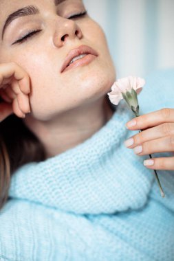 Kapalı stüdyo portresi. Açık dudakların yanında karanfil tutan güzel bir genç kadın. Cilt bakımı kavramı, doğal malzeme, hassas güzellik tedavisi, gözler kapalı..