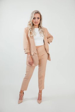 Bak kitap, sarışın, uzun saçlı, hoş bir kadın şık giyinen, beyaz arka planda bej takım giyen, sandalyede oturan, stüdyo fotoğrafı çeken