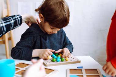 Oyun odasının kapanış masasında renkli yapıcı detaylarını katlayan küçük sevimli bir çocuk. Mantık ve zeka geliştiren anaokulu öğrencileri için ilginç bir oyun. Anaokulundaki akranlarla iletişim.