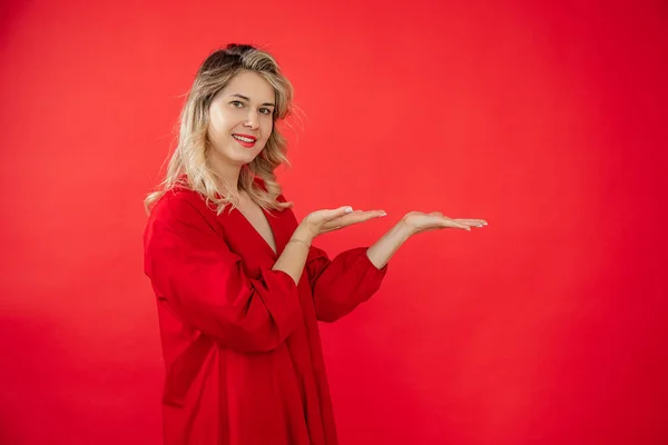 鮮やかな赤いドレスの若い女性の笑顔の肖像画立って 結果で手を指す赤の背景に孤立した 現代的な広告 無料のコピースペース ファッション 美容業界 — ストック写真