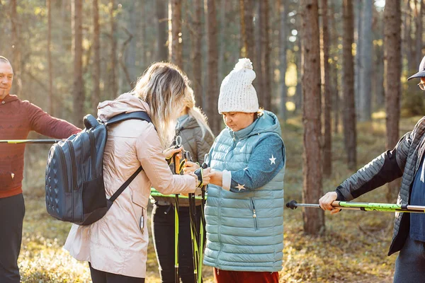 Woman coach, sports trainer with group of people showing good posture of hands and legs for Nordic walking with sticks in forest. Exercises hiking education for senior people. Weekend activity