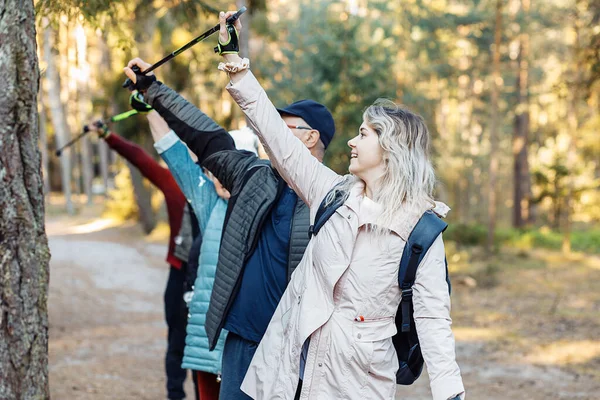 Group of people holding Nordic trekking poles in the air on trek while hiking in the forest, looking up. Exercises activity education course of different ages for health, breathing, posture technic