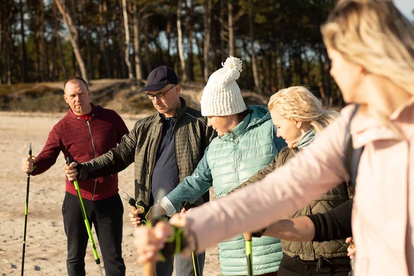 Close-up of leader woman and people group making Nordic walking with professional trekking sticks at the beach. Exercises education, arm technic and leg postures. Vacation activity for campers.