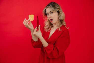 Baştan çıkarıcı, ağzı açık sarışın kadın kırmızı arka planda kırmızı biber ve patates cipsi tutuyor. Fast food atıştırmalığı seçimi ve vücut pozitifliği. Abur cubur pişirmek. Sağlıksız yiyecekler. Boşluğu kopyala