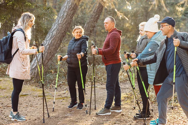 Professional woman coach, trainer with group of people teach Scandinavian, Nordic walking exercises with sticks in the forest, nature. Exercises hiking education for senior people. Vacation activity