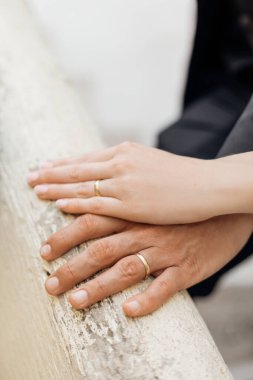Cropped photo of hands of loving couple with wedding rings. Brides hand covering grooms hand on white railing. Wedding, celebration, love, ceremony, newlyweds, marriage. Vertical, selective focus. 