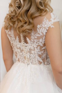 Back view of young woman bride with long wavy fair hair wearing white wedding embroidered dress with tender floral patterns decorated with pearls beads. Wedding, ceremony, fashion, design. Vertical.
