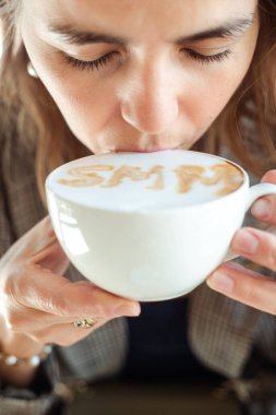 Young business woman drink hot flavored coffee with white foam with pleasure and closed eyes closeup. Social media marketing, SMM, promotion, delicious drinks in coffee house, meal time.