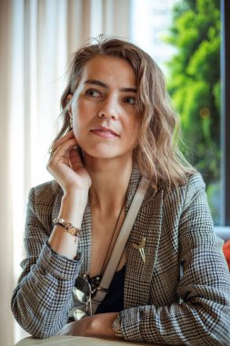 Portrait closeup of cute young businesswoman with nice makeup and accessories in stylish blazer sitting and looking away. Urban lifestyle, rest in cafe, thoughtful lady, successful people.
