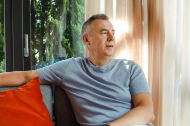 Mature thoughtful business man sitting on soft chair in cafe and looking at window. Handsome gray haired 50 years old man rest in cafe. Modern lifestyle, business people, public catering, relaxation.