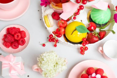 Pink and white sugar treats and berry, fruit desserts on cake stand, teapot on white table in candy shop or cafe. Birthday, valentines or wedding festive event. No sugar, vegan food. Top view