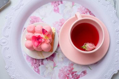 Sugar sweet pink neo cube ball velours mousse cake dessert with butterfly decoration on plate on table near cup of tea with rose bud and petals. Dessert table wedding festive event party. Top view