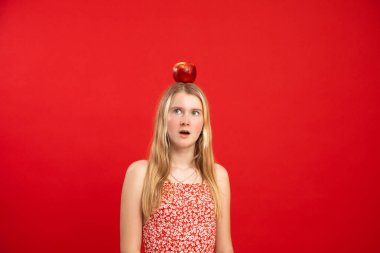 Portrait of blonde shocked, creative, thoughtful, puzzled girl with open mouth, red apple on head, looking away. Genius student, education and learning new. New idea and creative work, brainstorming