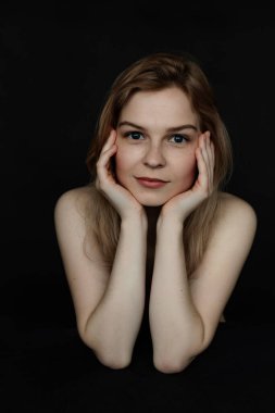 Siyah izole edilmiş arka planda kameraya bakan, pozitif, neşeli, mutlu ve hoş, genç, çıplak bir kadının dikey portresi. El ele tutuşan kadın, doğal güzellik ve yüz bakımı.