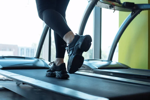 Photo of legs of woman in black comfortable sneakers and leggings running on treadmill at fitness gym. Girl do cardio workout on exercise machine. Weight loss, sport footwear, lifestyle.
