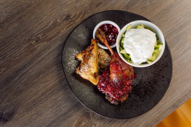 Kızarmış ördek eti, yeşil sebze salatası, beyaz krema ve böğürtlen sosuyla ahşap masanın üstünde. Ördek yemeği, parti ya da tatil menüsü. Paleo, keto diyeti. Üst görünüm, alanı kopyala
